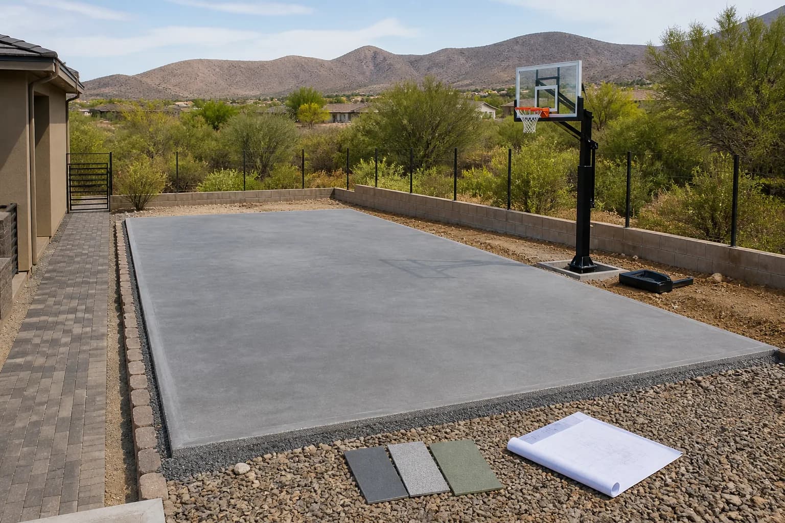 Outdoor basketball court construction planning scene with a prepared court pad, hoop system, surface samples, and residential access